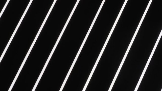 Contemporary interior ceiling featuring linear LED lamps. Minimalist geometric design light with glowing white diagonal lines against a dark background