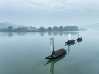 Obraz premium Three wooden boats quietly moored on a misty river with distant mountains in the background