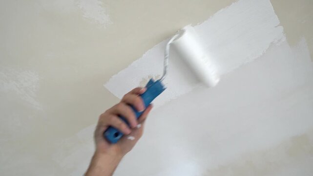 A worker applies white paint to the ceiling during an apartment renovation