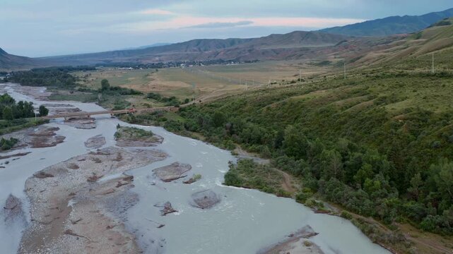 Braided river and gravel islands spread across valley as drone lifts upward over Chilik River, revealing expansive terrain, hills and distant mountains in Kazakhstan natural landscape