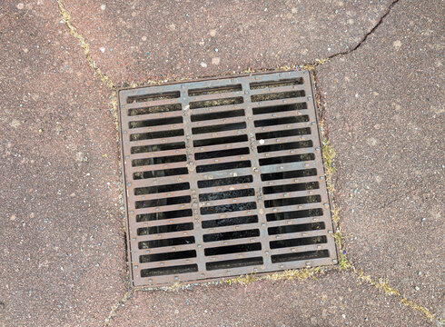 Square metal storm drain grate on an asphalt road with cracks
