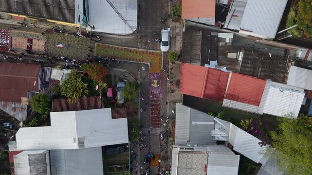 Aerial view of Easter procession during Semana Santa in Concepci&oacute;n de Ataco, El Salvador, with colourful alfombras de aserr&iacute;n, religious statues, and community celebrations in a vibrant cultural and s