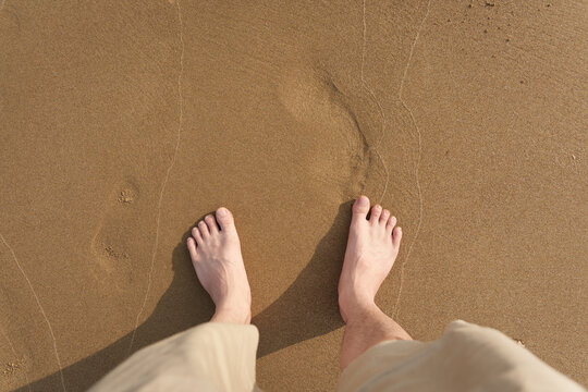 Male bare feet standing on sand beach in sunny day