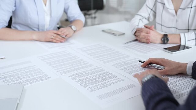 Business partners discussing contract terms, reviewing legal documents during an office meeting, focusing on agreement details and professional negotiation strategies