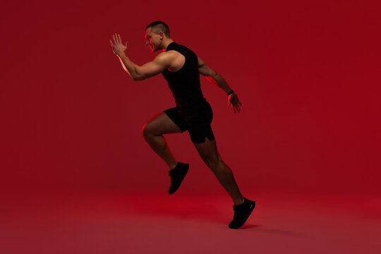 Athletic man sprinting in black sportswear against bold solid red studio background