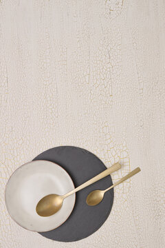 Minimal food background with golden plate and spoons on neutral surface, clean flat lay with copy space