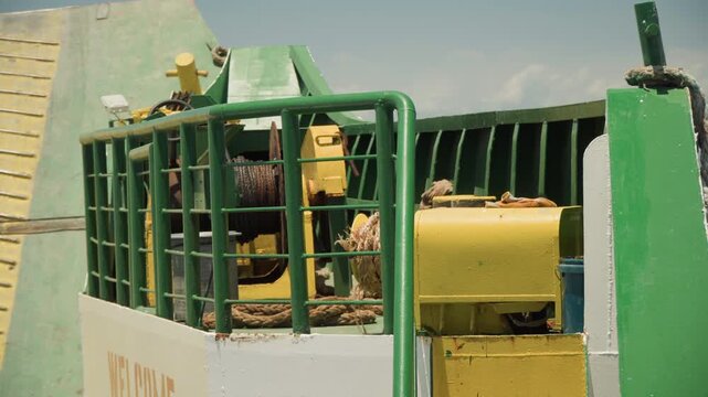 Green machine cage winch operator maintenance, closeup of metal drum, cable, gears, and hydraulic components on weathered construction equipment, worker in helmet inspects guard, gritty sunlight