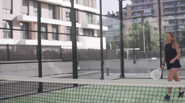 Active young woman playing padel tennis, returning the ball with a controlled forehand shot near the net. Female player demonstrating technique, focus, and agility on a modern outdoor court. Concept