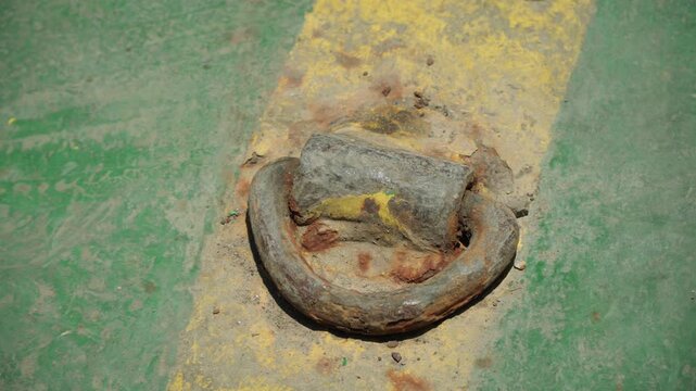 Rusty metal ring on painted concrete, closeup showing heavy corrosion, flaking paint and gritty dust along faded yellow stripe tactile patina evokes maritime workshop and repair context, ideal