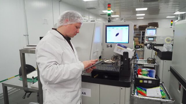 Engineer at workplace. Employee of high-tech LED lamp and lighting fixture manufacturing plant configures the installed equipment to ensure the smooth and precise operation of printing press.