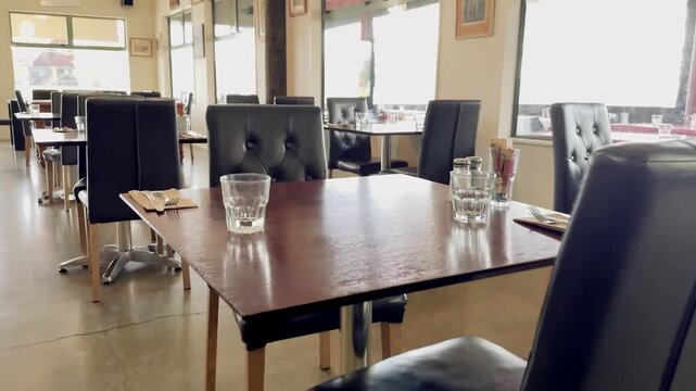 Camera sliding forward through empty restaurant interior with black leather chairs and wooden tables.