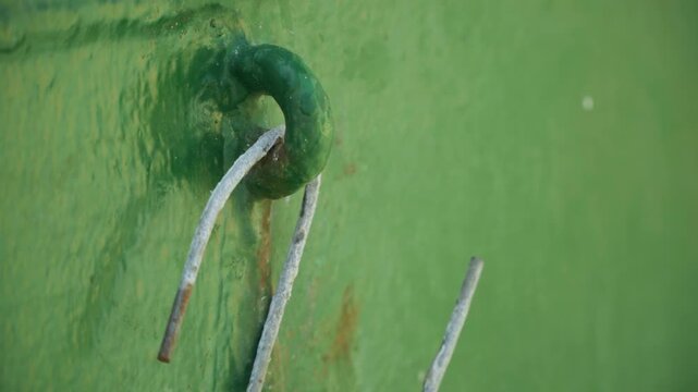 Closeup green metal eyelet with frayed white wire threaded into painted hull, subtle scratches, fresh paint texture, maritime hardware detail, shallow depth of field, natural light glow