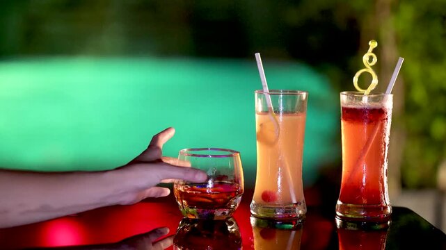 Close-up of hand picking up a martini glass with alcoholic drinks on table.