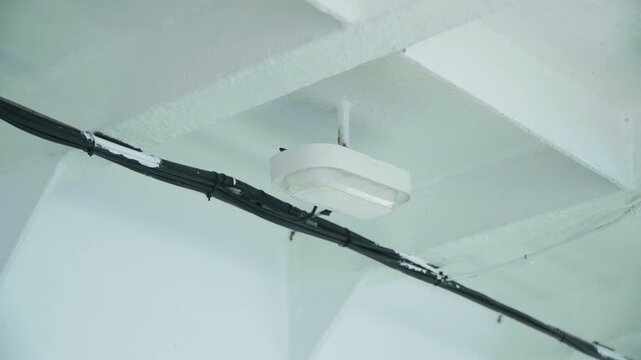 Closeup of smoke detection system. Interior view highlighting smoke detector and conduit details. Minimalist industrial environment featuring smoke detector and visible electrical conduits