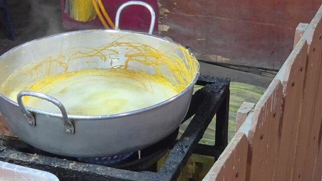 Chef Pouring Egg Yolk into a Boiling Pot to Create Golden Threads (Foi Thong) for a Traditional Thai Dessert