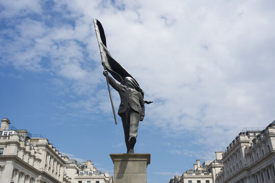 Banksy artwork statue in Waterloo Place in London of a man holding a flag that is covering his face. 