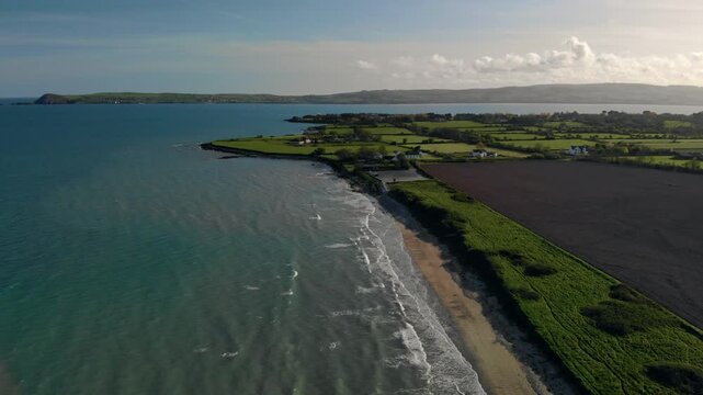 Drone glides smoothly over serene Irish coastline, revealing lush green fields and tranquil atmosphere, inspiring a sense of calm and natural beauty, perfect for travel and wellness marketing.