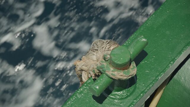 Hermit crab on green railing, barnacled shell clinging to weathered cleat, sunlit spray and churning ocean below, textured metal with rust and algae, closeup detail showing motion, salt residue,