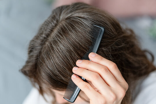 A young woman stares at her premature gray hair with disbelief and frustration. The mature adult feels angry and cheated by early aging signs appearing. Mother wonders why silver came so soon.