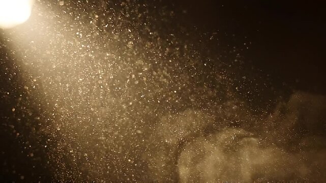 Golden dust particles illuminated by a bright light source creating a bokeh effect and a sense of magical atmosphere with a dark background