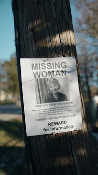 Missing woman poster with reward notice pinned to wooden utility pole in suburban street during daylight