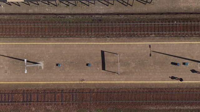 Top down aerial view of an empty railway platform with parallel train tracks and long shadows