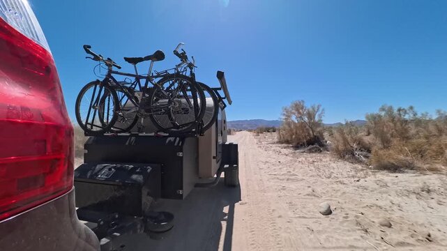 A teardrop camper trailer follows an SUV down a sandy road in Baja California, searching for a place to camp among cacti.