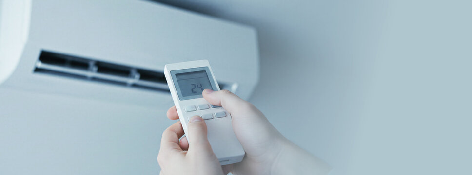 Woman hand using remote control to adjust air conditioner temperature. Climate control and thermal comfort regulation in modern room. Household appliance maintenance and summer cooling system. Banner