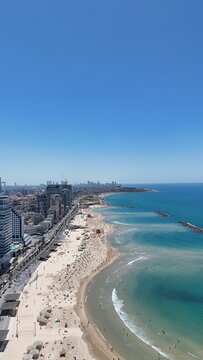 Aerial 4K view of Tel Aviv coastline, bustling promenade, luxury hotels, and sandy beach on a sunny day, Israel
