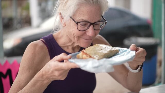 Mature woman eats shrimp tacos from a taco stand in Baja California Mexico while savoring her lunch in a casual setting