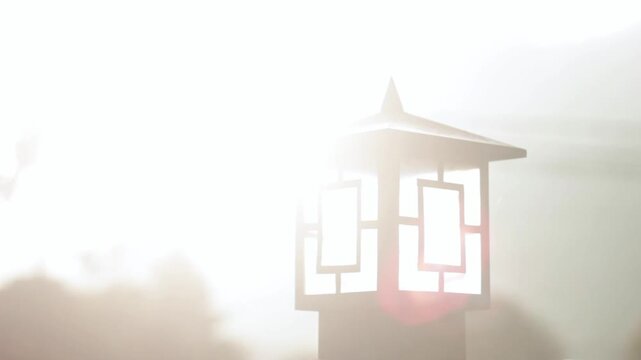 Outdoor Garden Lantern Lamp with Bright Morning Sunlight and Lens Flare. A silhouette of a classic style outdoor garden lantern lamp captured against an overexposed bright sky. 