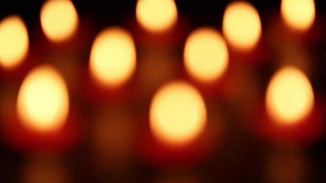 Rows of lit candles with warm orange and yellow bokeh fill dark background, camera focus slowly drifts across glowing flames, creating calm meditative candlelight atmosphere.