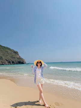 Woman stands on sandy beach in summer weather by the ocean with mountains in the background during midday