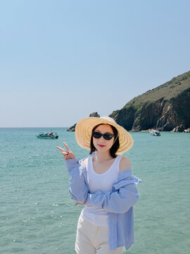 Young woman enjoys a sunny day at the beach in Asia while wearing a large hat and sunglasses