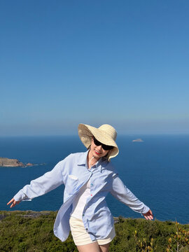 Young woman enjoys a sunny day at the beach with ocean view wearing a straw hat and sunglasses while posing for the camera