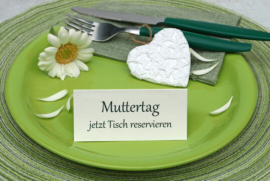 Gr&uuml;ner Teller mit Besteck, wei&szlig;er Blume, Herz  und Karte mit Text 'Muttertag jetzt Tisch reservieren'