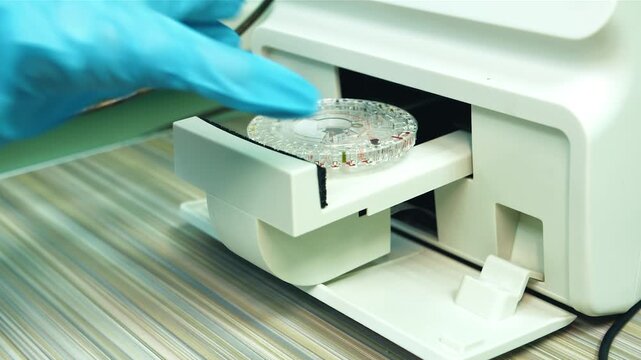 Hand in blue glove takes away petri dish from incubator drawer. Circular agar plate on instrument tray being slid into warming chamber on striped benchtop, sterile clinical setting with technician