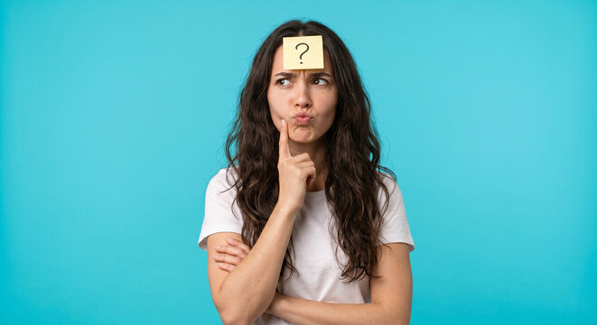 Confused young woman thinking with question mark sticky note on forehead isolated on blue background