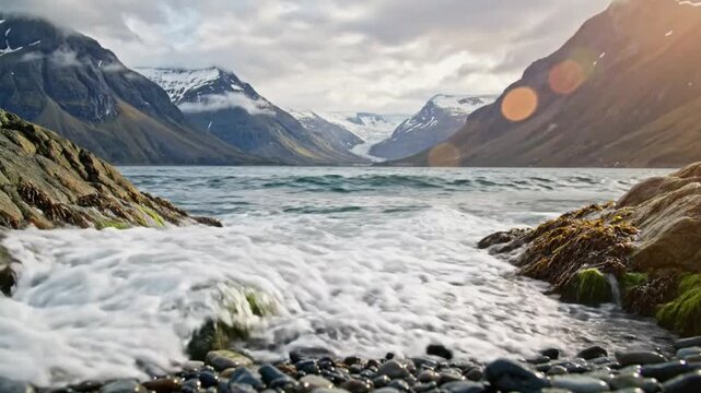 Waves crashing between moss-covered rocks in a fjord with mountains, glacier and sunny sky