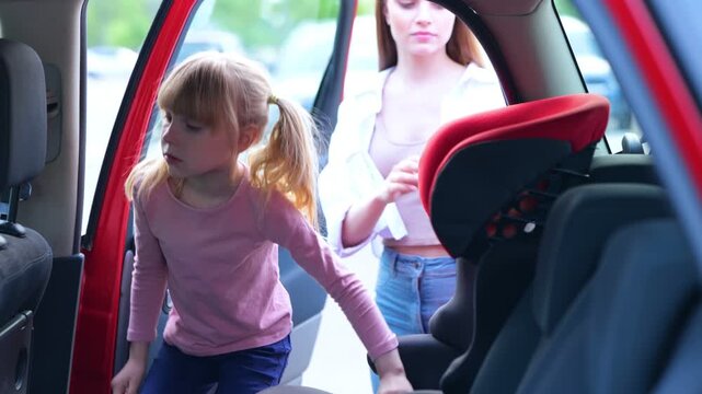 Young woman fastening little female kid with a seat belt in the back seat in the car before journey. Family, transport, trip, safety and parenthood concept. Real time