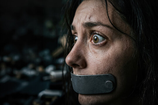 A close-up profile of a terrified woman with a metallic gag