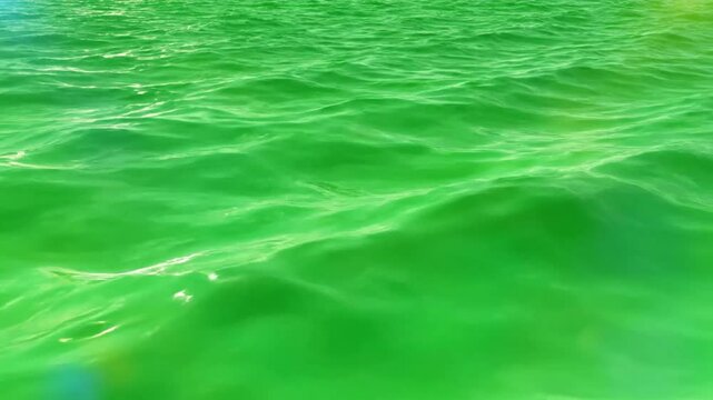 Mesmerizing close-up of emerald green water with gentle waves reflecting sunlight on a tranquil day
