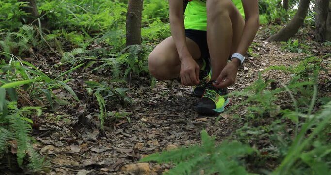 Woman ultramarathon runner tying shoelace before running in tropical rainforest  