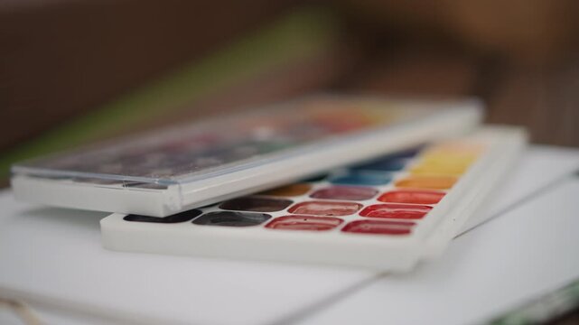 Watercolor palette on sketchbook pages, paint pans exposed, subtle color gradations, wet mixing on paper, close focus on palette edge, creative workspace vibe, artist practicing strokes, quiet studio