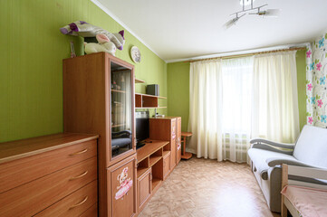 Fototapeta premium cozy room with lime-green walls, wooden furniture wall unit, plush toys on top, cream curtains, light sofa, floral wallpaper accent, TV, soft lighting, warm and child-friendly atmosphere