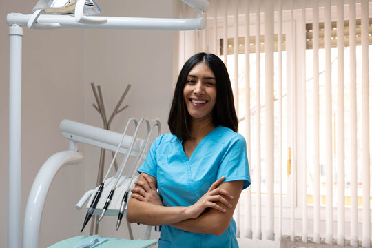 Hispanic woman dentist smiling, proudly standing in her modern dental clinic