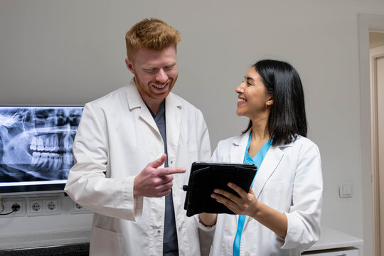 Dental professionals smiling and discussing patient records on a digital tablet in a modern clinic