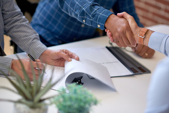 Business people, meeting or handshake with documents for contract agreement or partnership. Group, employees or colleagues shaking hands with paperwork or signature for b2b or onboarding in workplace