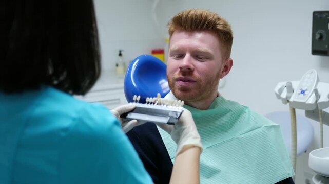 Female dentist using a shade guide to select a dental crown for her smiling patient