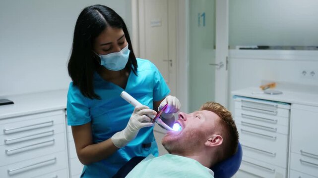Professional female dentist performs a dental procedure on a male patient in a modern clinic
